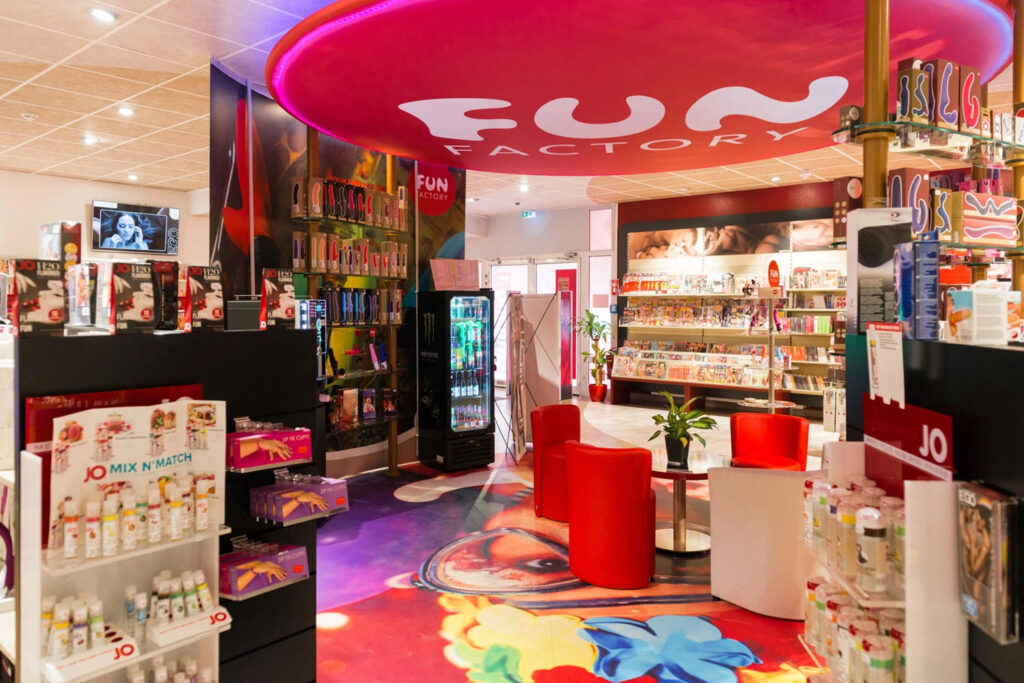 Bunter Erotikshop mit rotem Sitzbereich und Regalen voller Produkte und bunter Deko